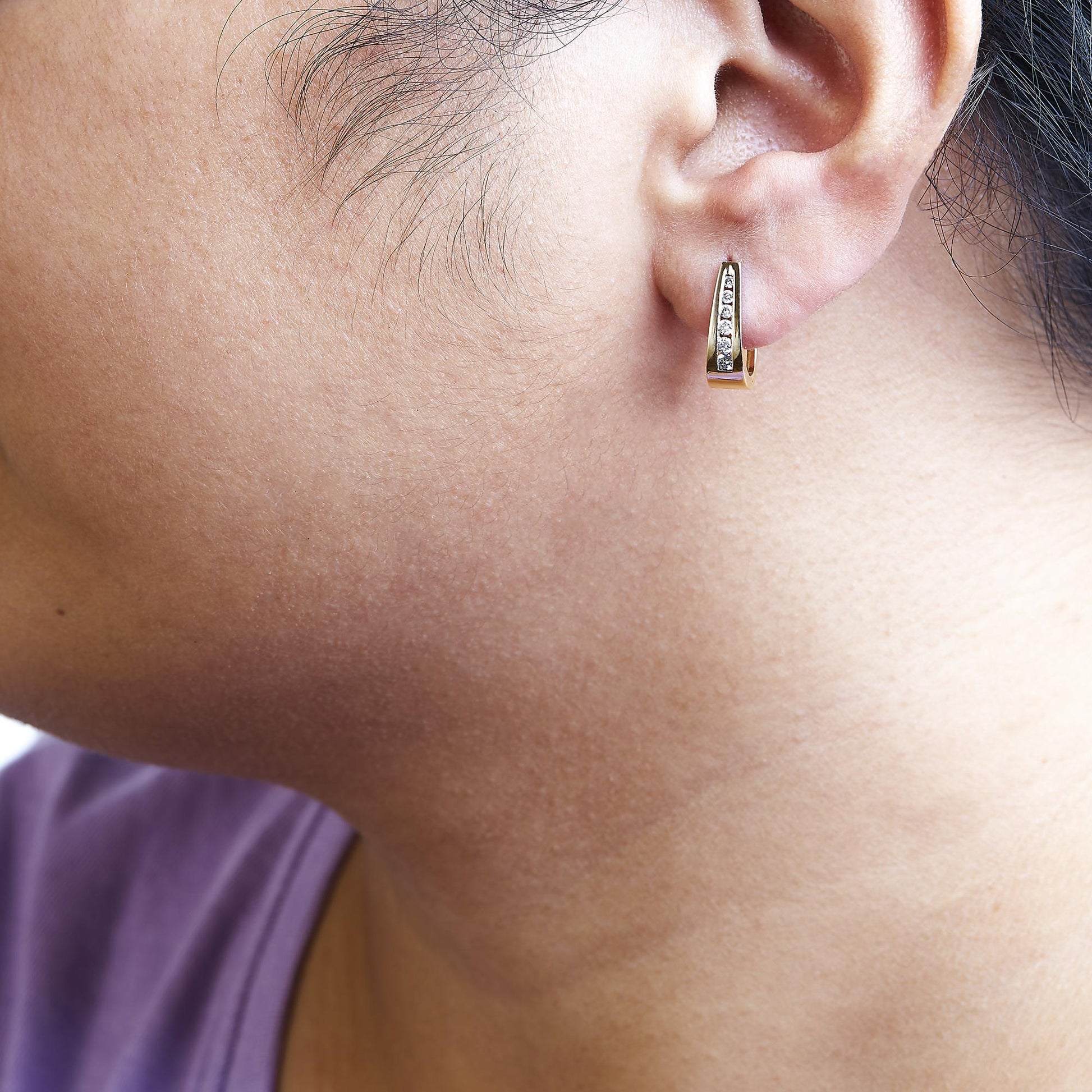 Close-up side view of a yellow metal earring with a channel setting of white round gemstones, worn on a model.