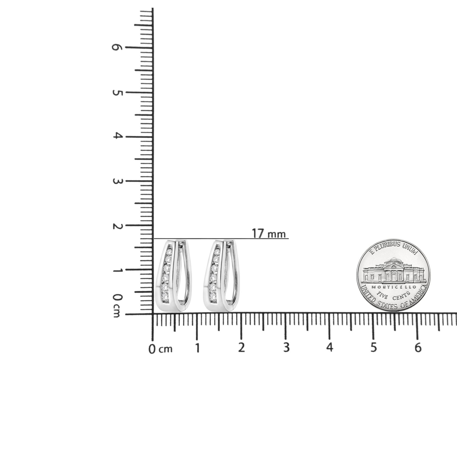 Pair of white metal earrings with a tapered design and a row of round white gemstones in channel setting, shown from the front on a ruler for size reference.