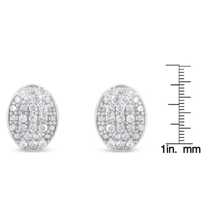 Front view of a pair of white metal oval earrings with round white gemstones in prong settings, shown next to a ruler for size reference.