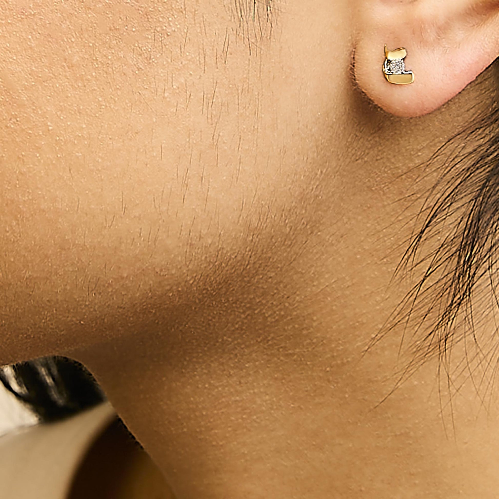 Close-up side view of a yellow metal earring with two white round gemstones in prong settings, worn on a model's ear.
