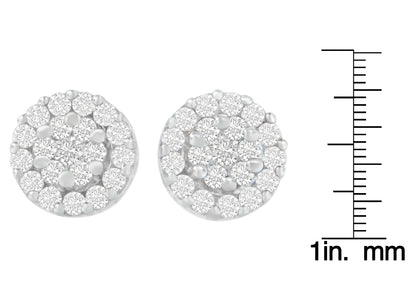 Close-up front view of round white metal earrings with clustered white gemstones in prong settings, shown next to a ruler for size reference.