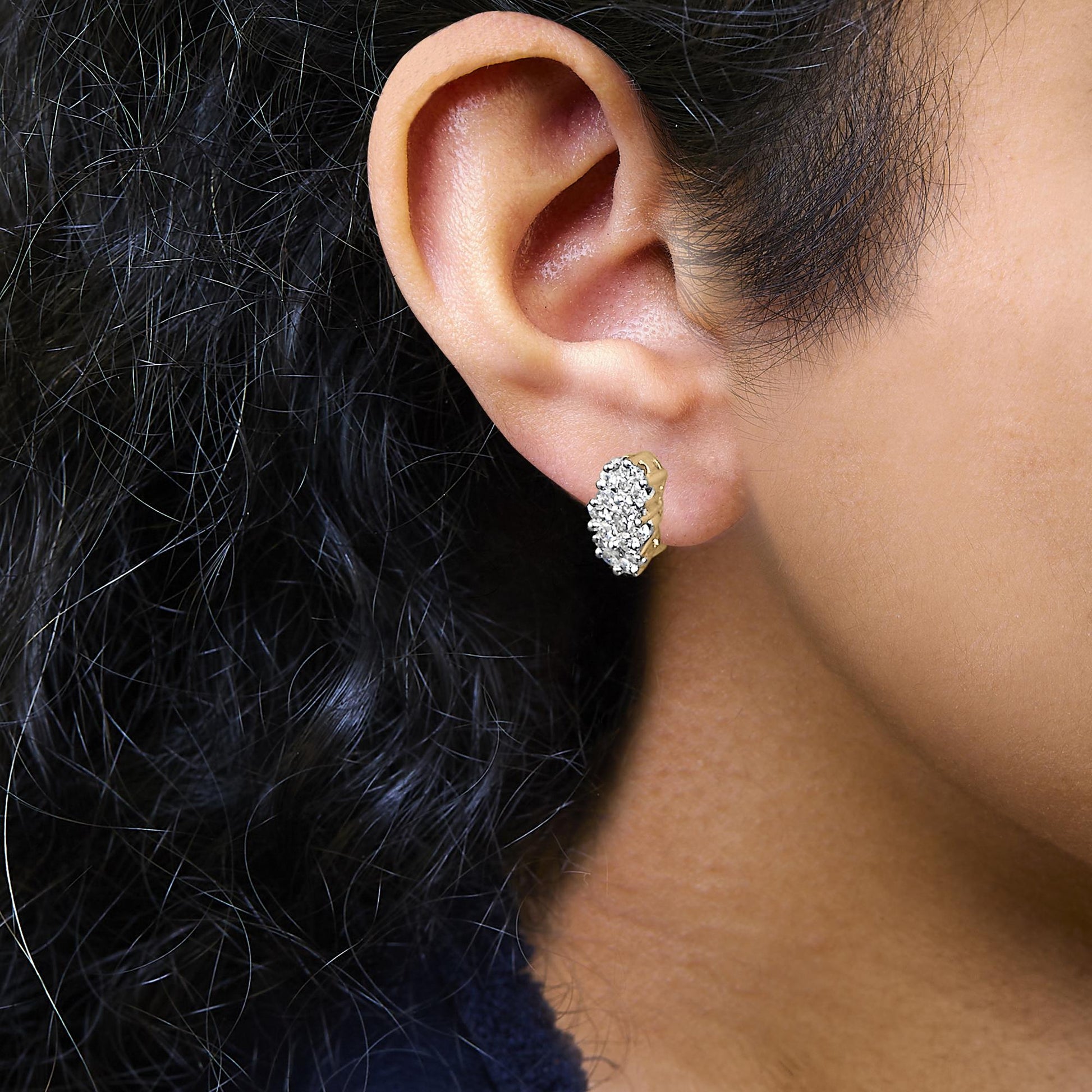 Close-up side view of a yellow metal earring with multiple white round gemstones in prong settings worn on a model's ear.