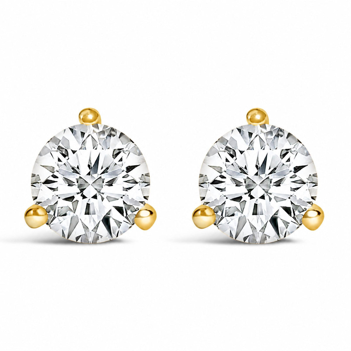 Close-up front view of a pair of yellow metal stud earrings, each featuring a round white gemstone in a three-prong setting.
