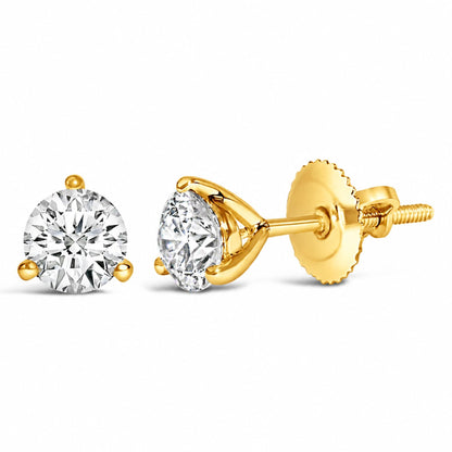 Close-up front and side view of a pair of yellow metal stud earrings featuring round white gemstones in a three-prong setting. The earrings are shown laying on a flat surface.