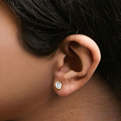 Close-up side view of a model wearing a single yellow metal stud earring with a round white gemstone in a three-prong setting.