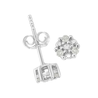 Close-up image of a pair of white metal stud earrings with round white gemstones in a prong setting, one showing the front cluster and the other showing the post and butterfly back, shot from an angled top-down perspective.