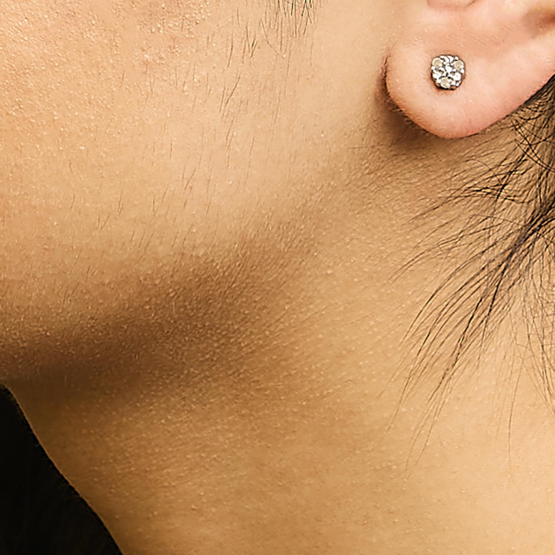 Close-up side view of a white metal earring with six round white gemstones in a cluster prong setting, worn on a model's ear.