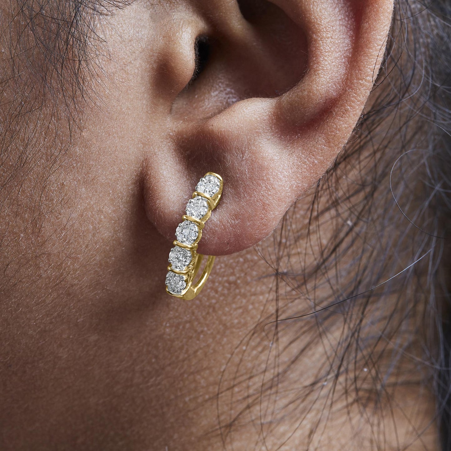 Close-up side angle of a yellow metal earring with a vertical row of round white gemstones in prong settings, shown worn on a model.