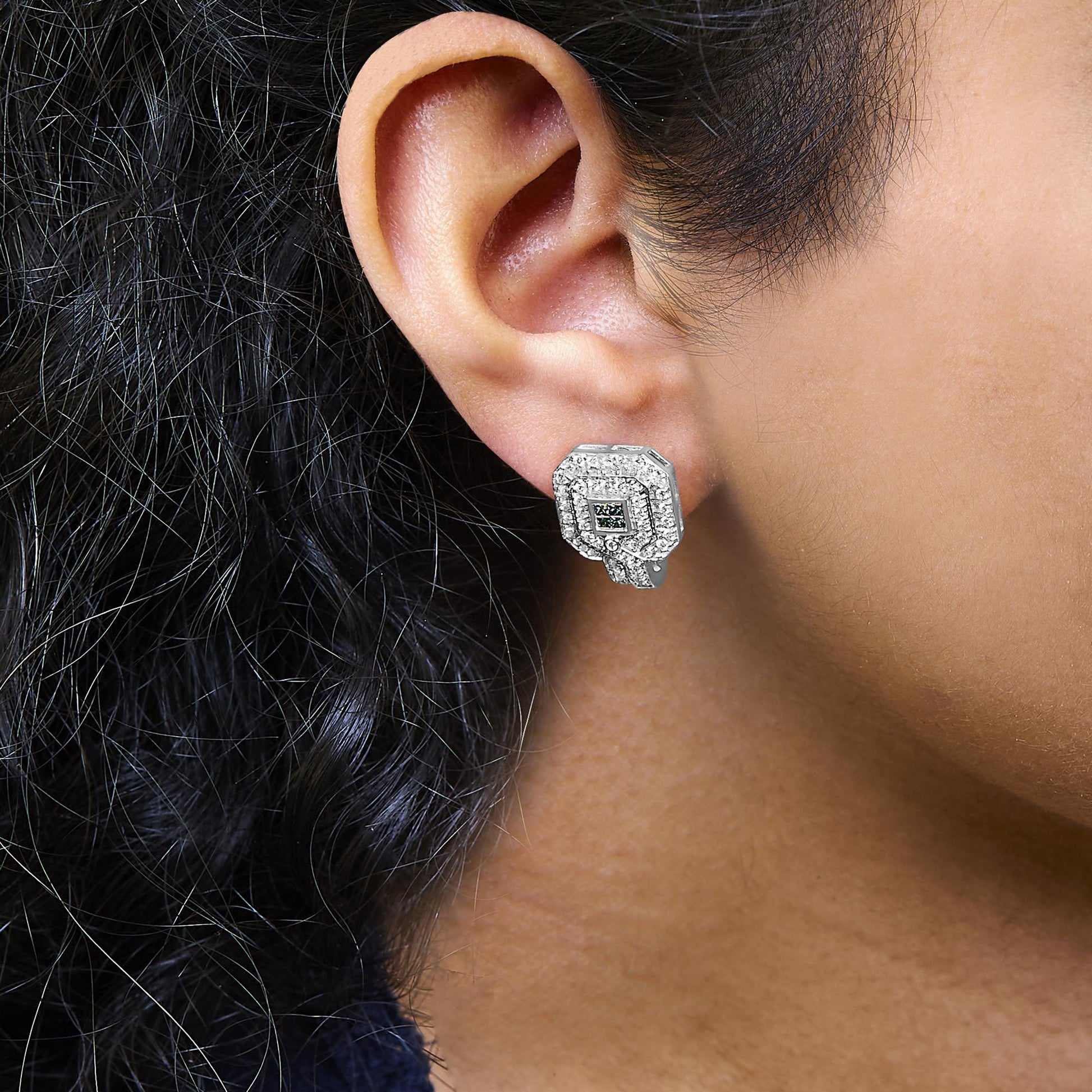 Close-up side view of a white metal earring with round white gemstones in a pave setting surrounding a cluster of blue gemstones in an invisible setting, worn on a model's ear.