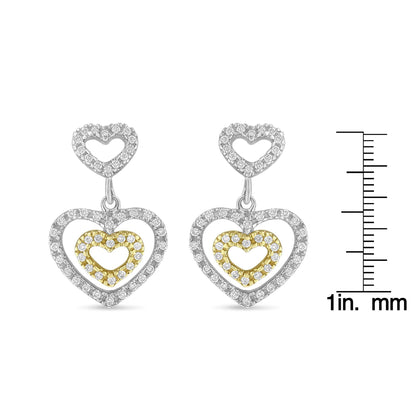Front view of two-toned heart-shaped dangling earrings with pave set round white gemstones, displayed next to a ruler for size reference.