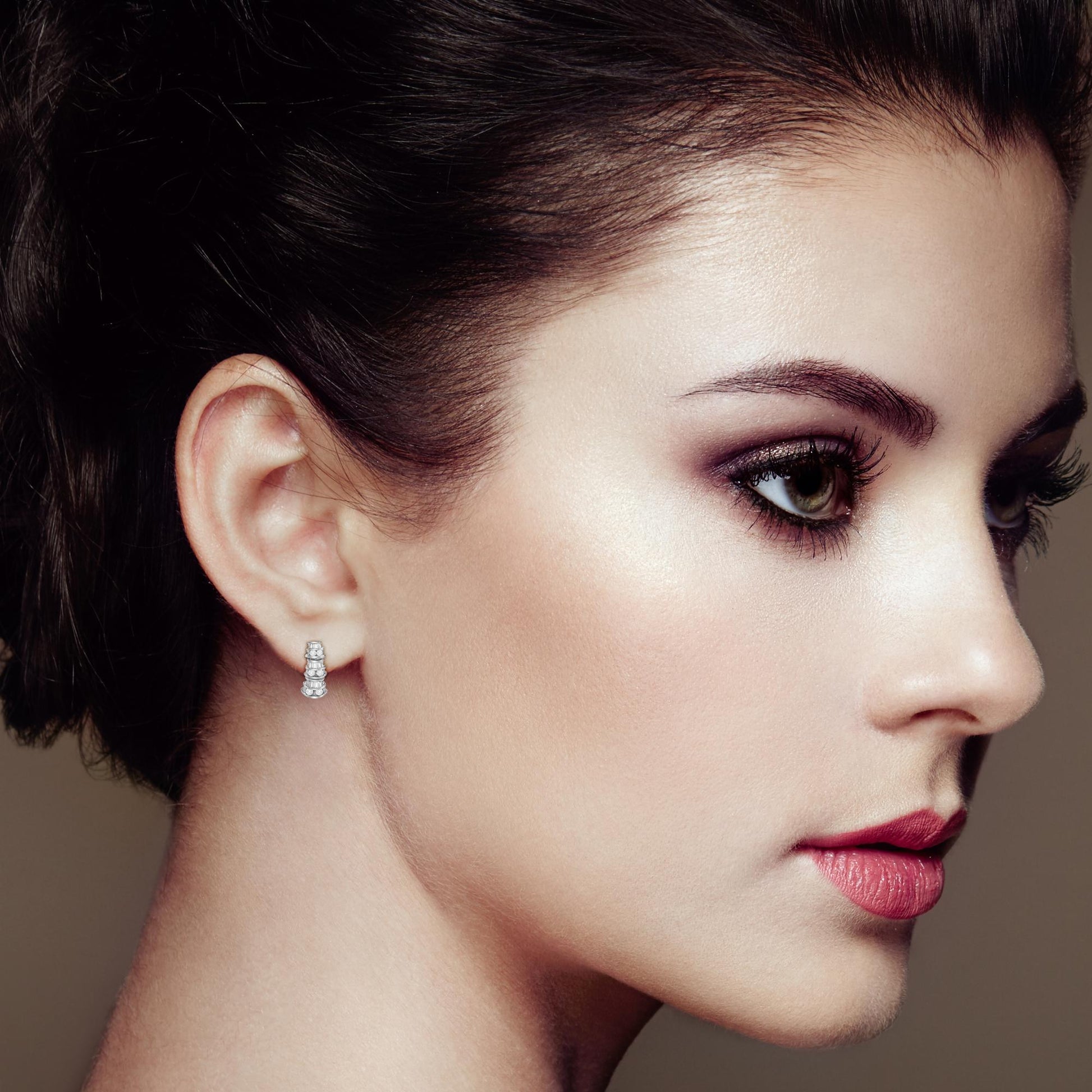 Close-up side profile of a model wearing white metal earrings with round and baguette-shaped white gemstones in a channel setting.