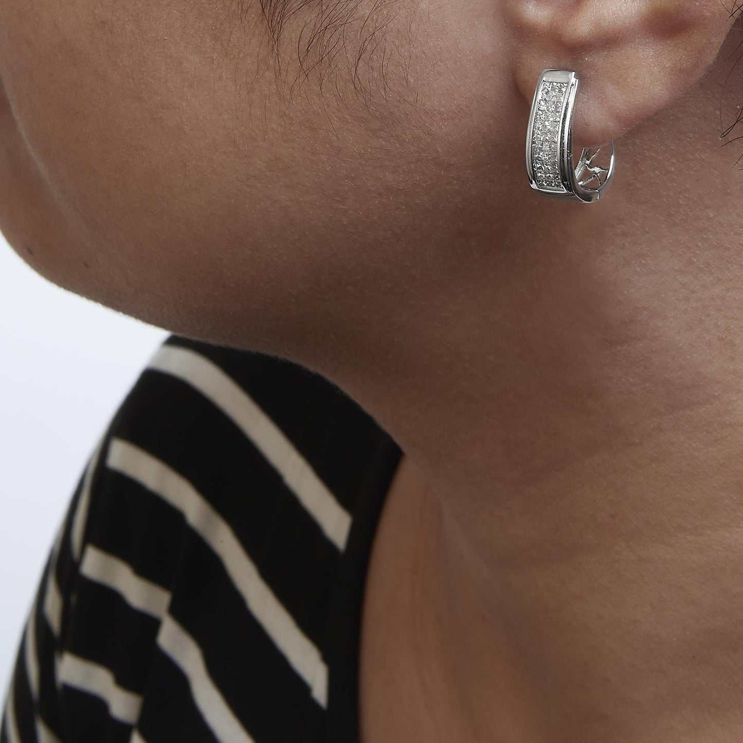 Close-up side view of a model wearing a white metal earring featuring a curved rectangular shape adorned with multiple small white gemstones in an invisible setting.
