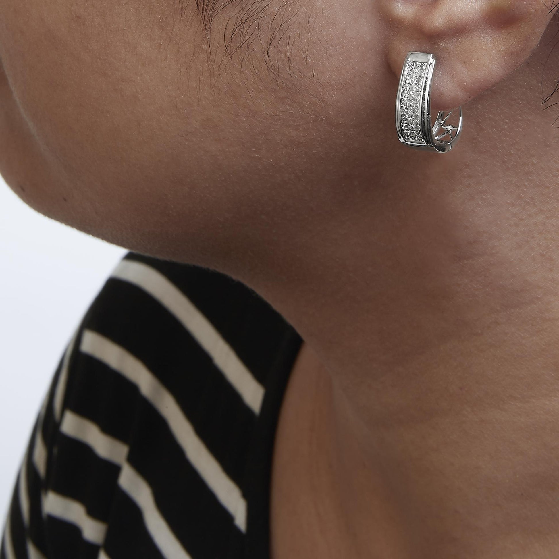 Close-up side view of a model wearing a white metal earring featuring a curved rectangular shape adorned with multiple small white gemstones in an invisible setting.