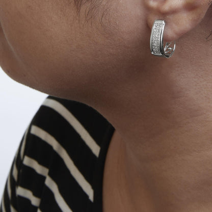 Close-up side view of a model wearing a white metal earring featuring a curved rectangular shape adorned with multiple small white gemstones in an invisible setting.