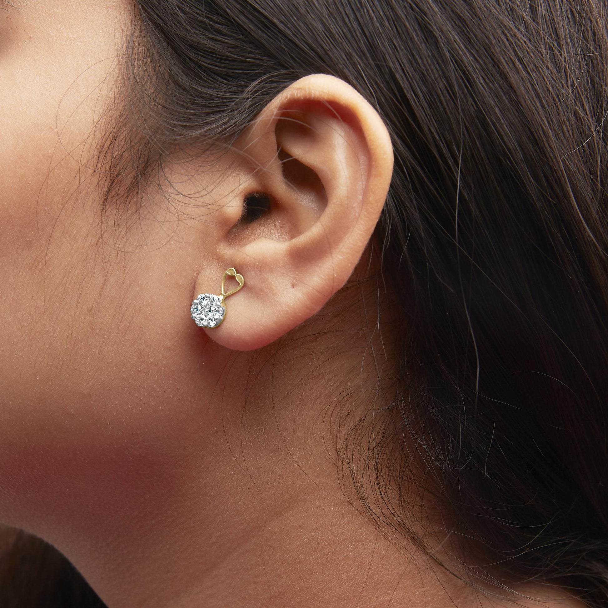 Close-up side view of a yellow metal earring with a cluster of round white gemstones in prong setting, worn on a model.
