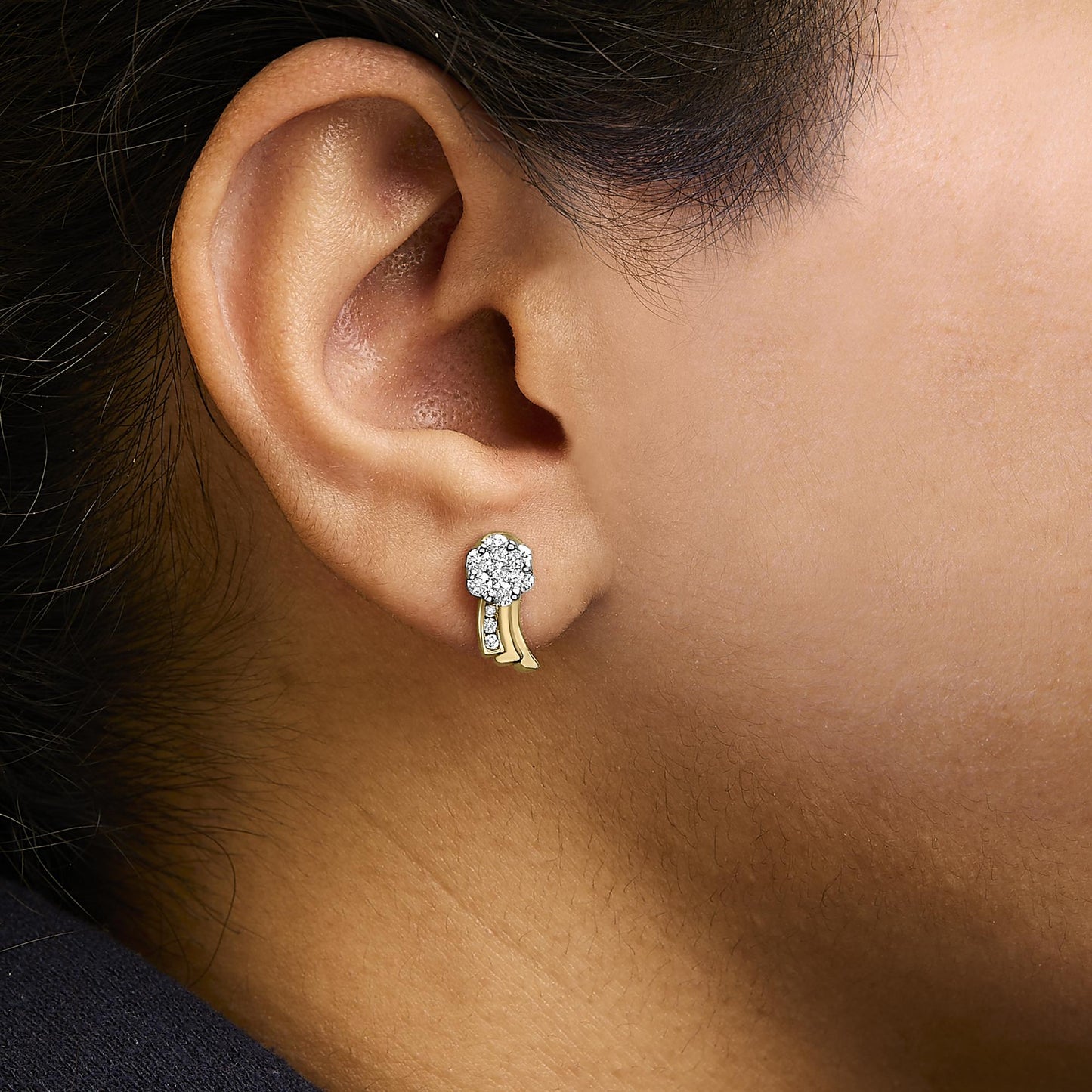 Close-up side view of an ear wearing a yellow metal earring with a cluster of round white gemstones in prong setting and three curved yellow metal strands below, two adorned with small white gemstones.