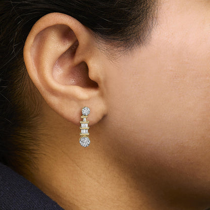 Close-up side view of a yellow metal earring on a model's ear, featuring white round gemstones in prong settings at the top and bottom, with white baguette gemstones in channel settings arranged vertically between them.
