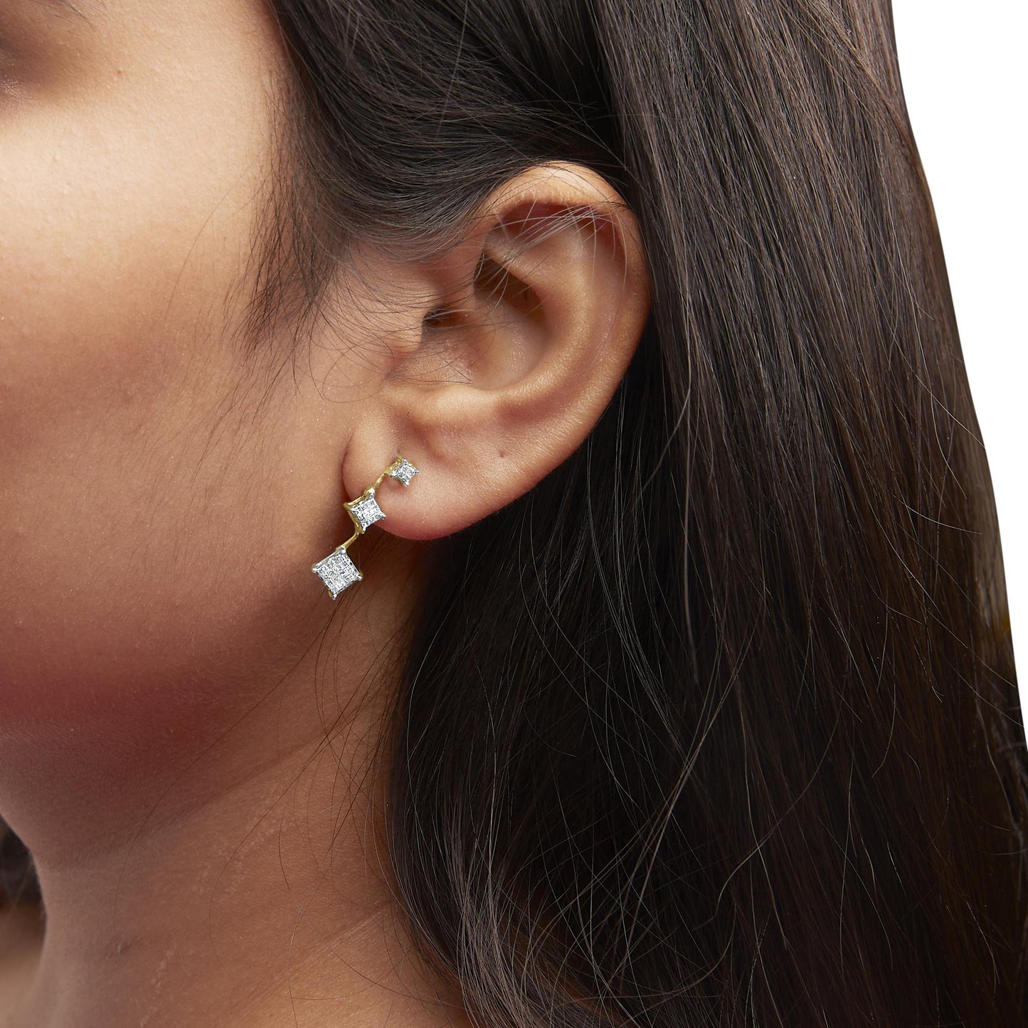 Close-up side view of a model wearing yellow metal earrings featuring multiple princess-shaped white gemstones in an invisible setting.