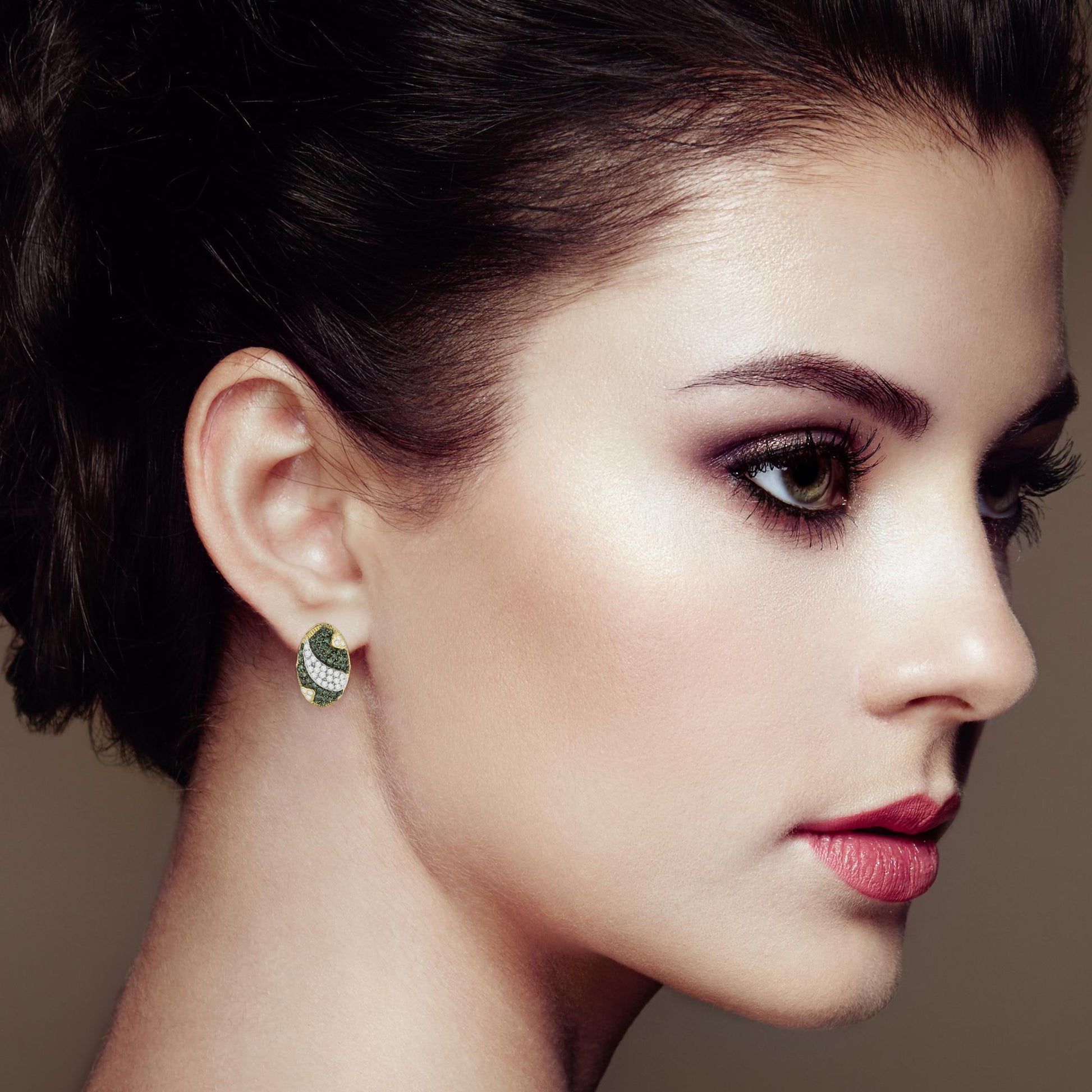 Side view of a model wearing yellow metal earrings with white and blue round pave-set gemstones in an oval design.
