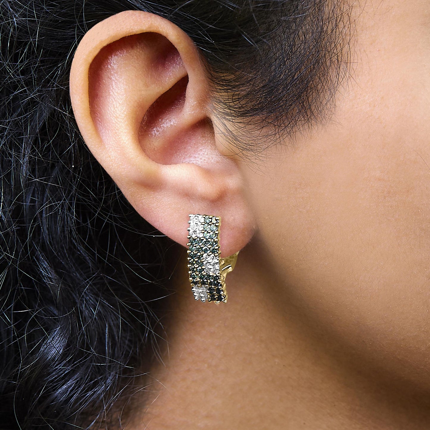 Close-up side view of a model wearing yellow metal earrings featuring pave-set round white and blue gemstones in alternating horizontal rows.