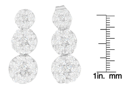 Front view of white metal triple cluster earrings with round white gemstones in prong settings, displayed next to a scale.