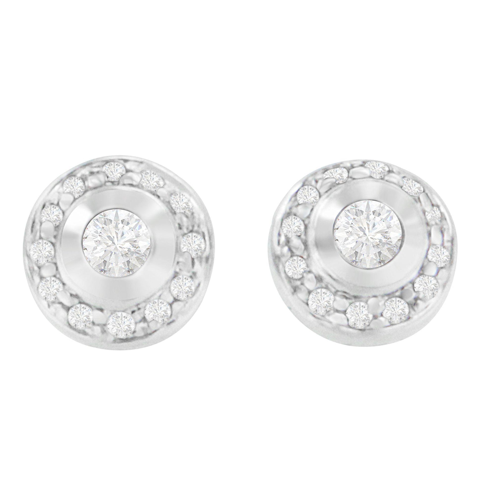 Front view of a pair of white metal round stud earrings, each featuring a central round gemstone in bezel setting surrounded by a circle of smaller round gemstones in prong settings.