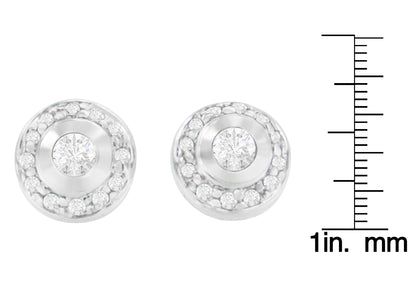 Front-facing view of a pair of white metal round earrings with central white gemstones in bezel settings surrounded by smaller white gemstones in prong settings, shown on a ruler for size reference.