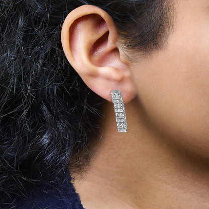 Close-up side view of a white metal earring with round prong-set and baguette channel-set white gemstones, worn on a model's ear.