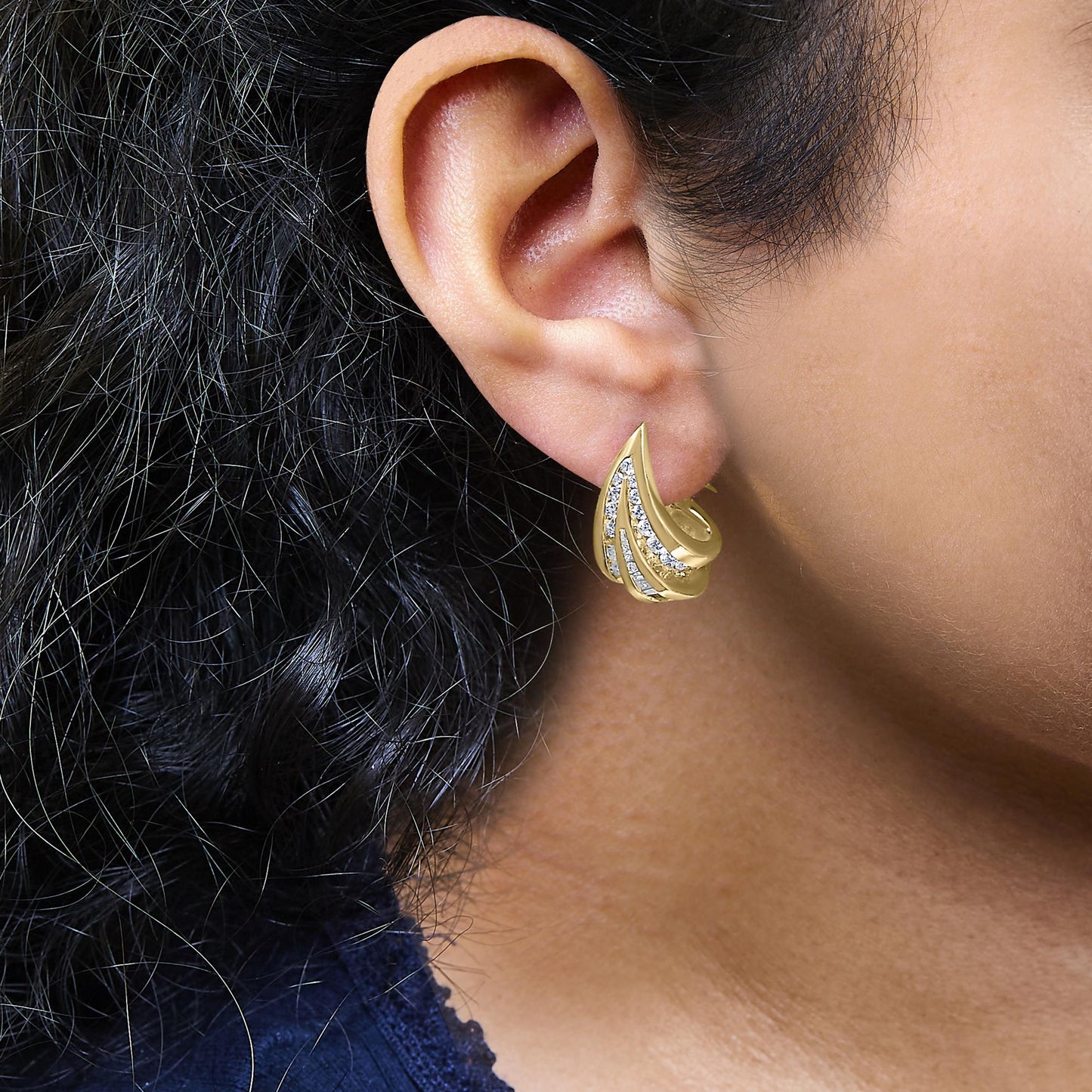 Close-up side view of a yellow metal earring on a model’s ear, featuring curved rows of white round and baguette-shaped gemstones in a channel setting.