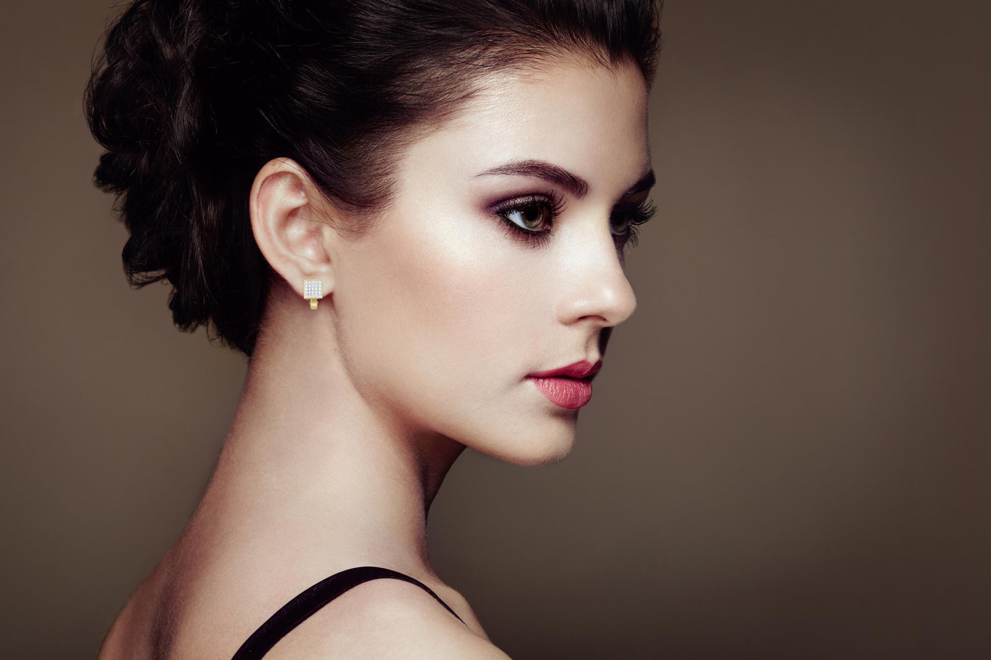 Side view of a model wearing square-shaped yellow metal earrings with multiple small white gemstones in an invisible setting.