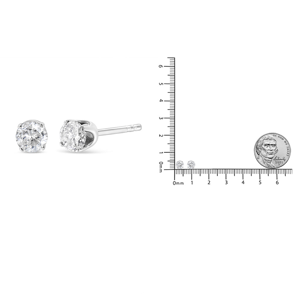 Pair of white metal stud earrings with round white gemstones in prong settings, shown from a side angle and positioned next to a ruler for size reference.