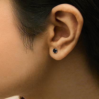 Close-up side view of a model's ear wearing a pair of white metal stud earrings featuring round black gemstones set in four prongs.