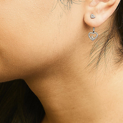 Close-up side view of a model wearing white metal heart-shaped stud earrings and matching dangling heart-shaped earrings with white gemstones in a pave setting.