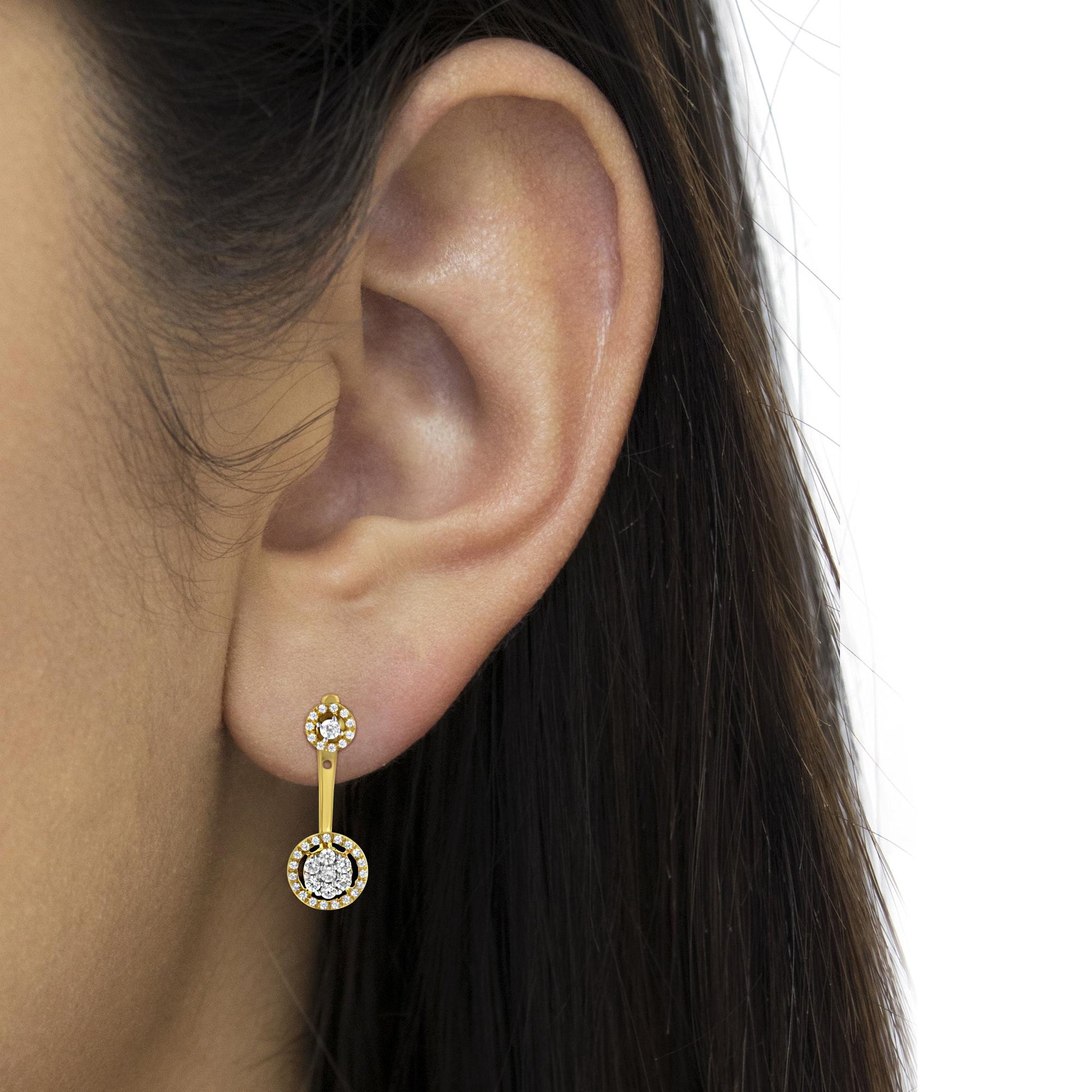 Close-up side view of a yellow metal drop earring on a model's ear featuring round white gemstones in prong settings at the top and bottom, connected by a slim bar.
