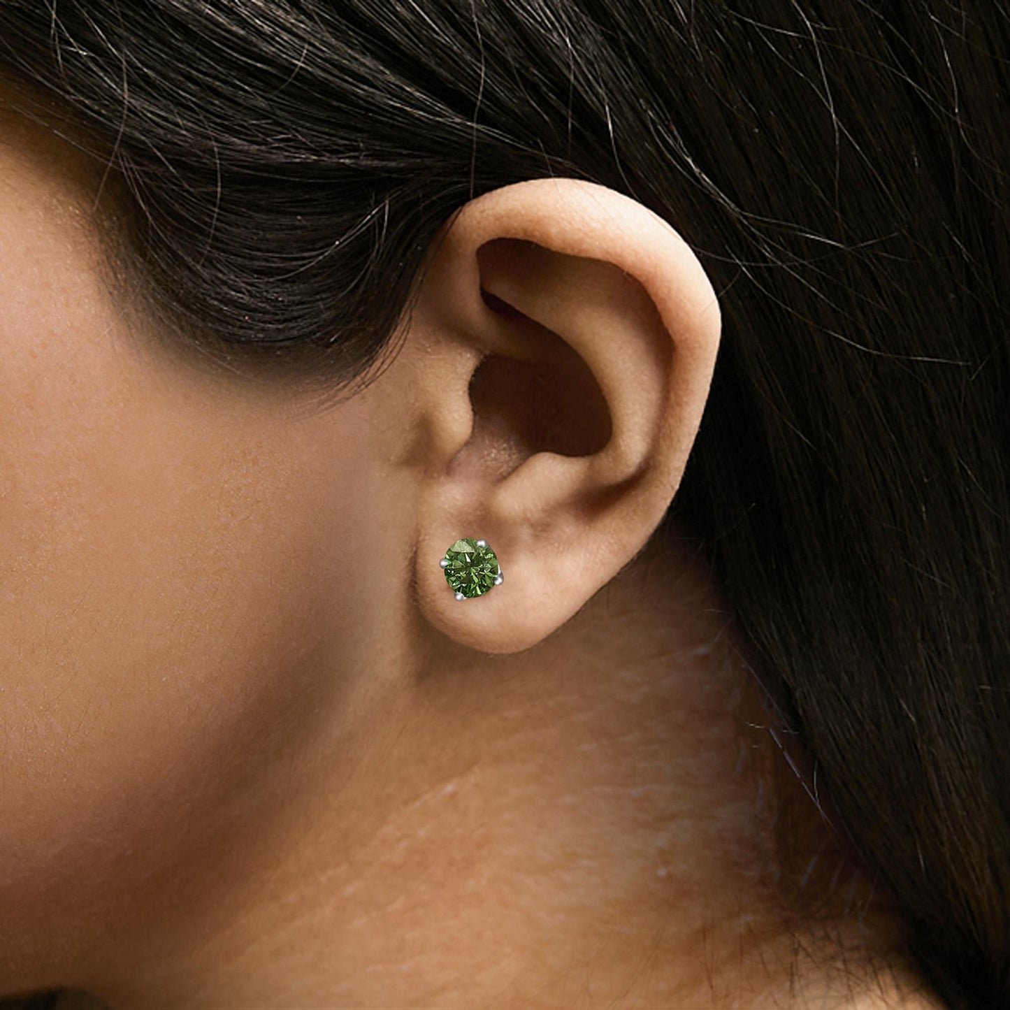Close-up side view of a model wearing white metal stud earrings with round green gemstones in 4-prong settings.