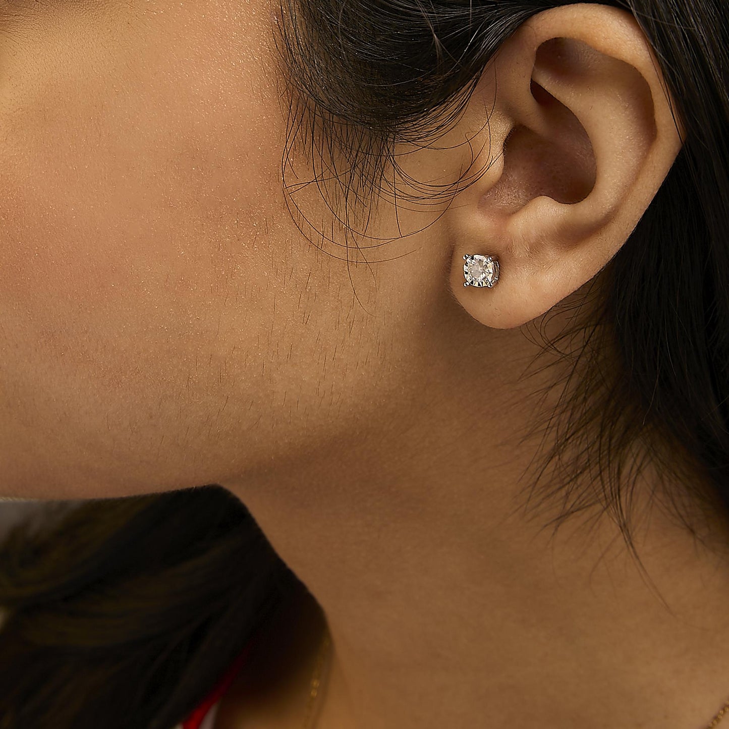 Close-up side view of a white metal stud earring with a round white gemstone in miracle setting worn on a model's ear.