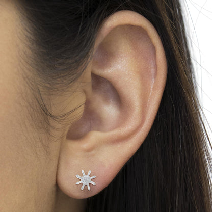 Close-up side view of a yellow metal earring on a model’s ear, featuring a circular cluster of small round white gemstones in the center with baguette-shaped white gemstones radiating outward.