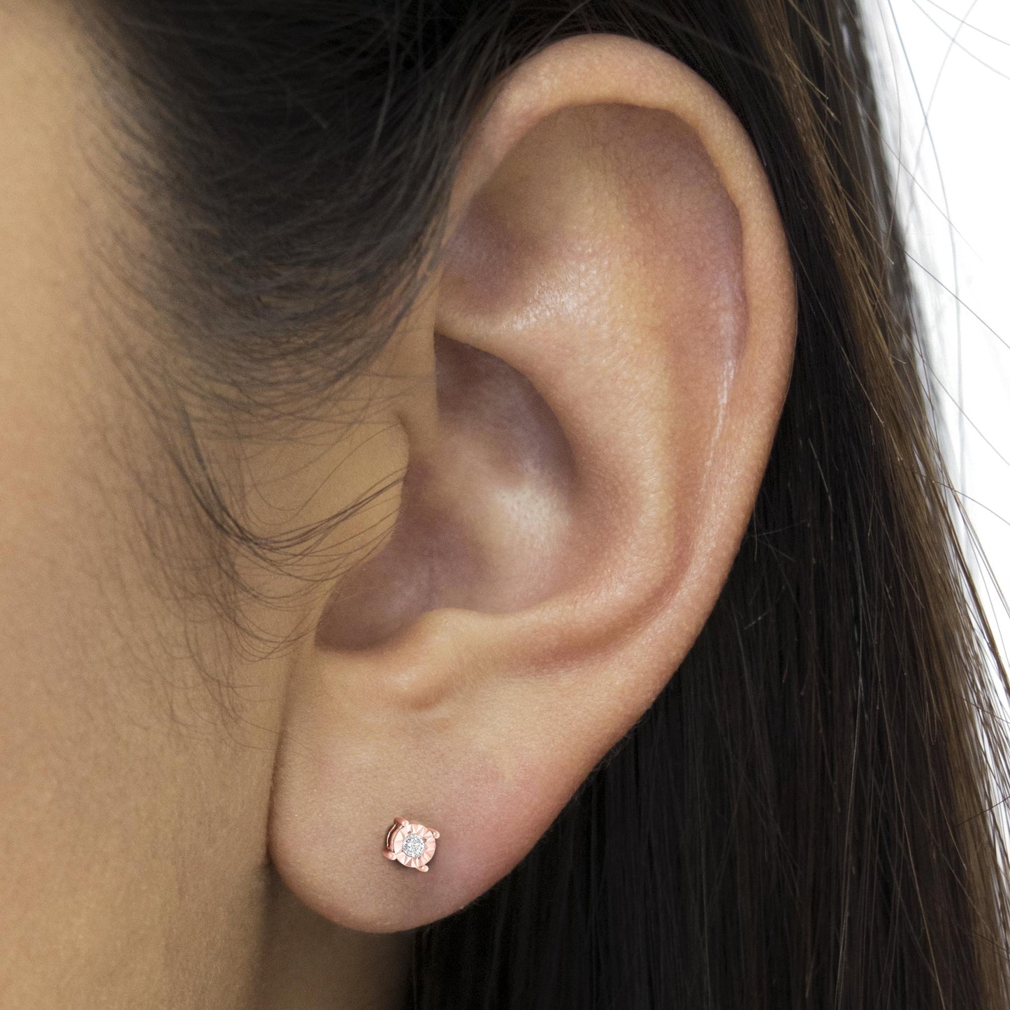 Close-up side view of a rose metal stud earring with a round white gemstone in miracle setting, worn on a model's ear.