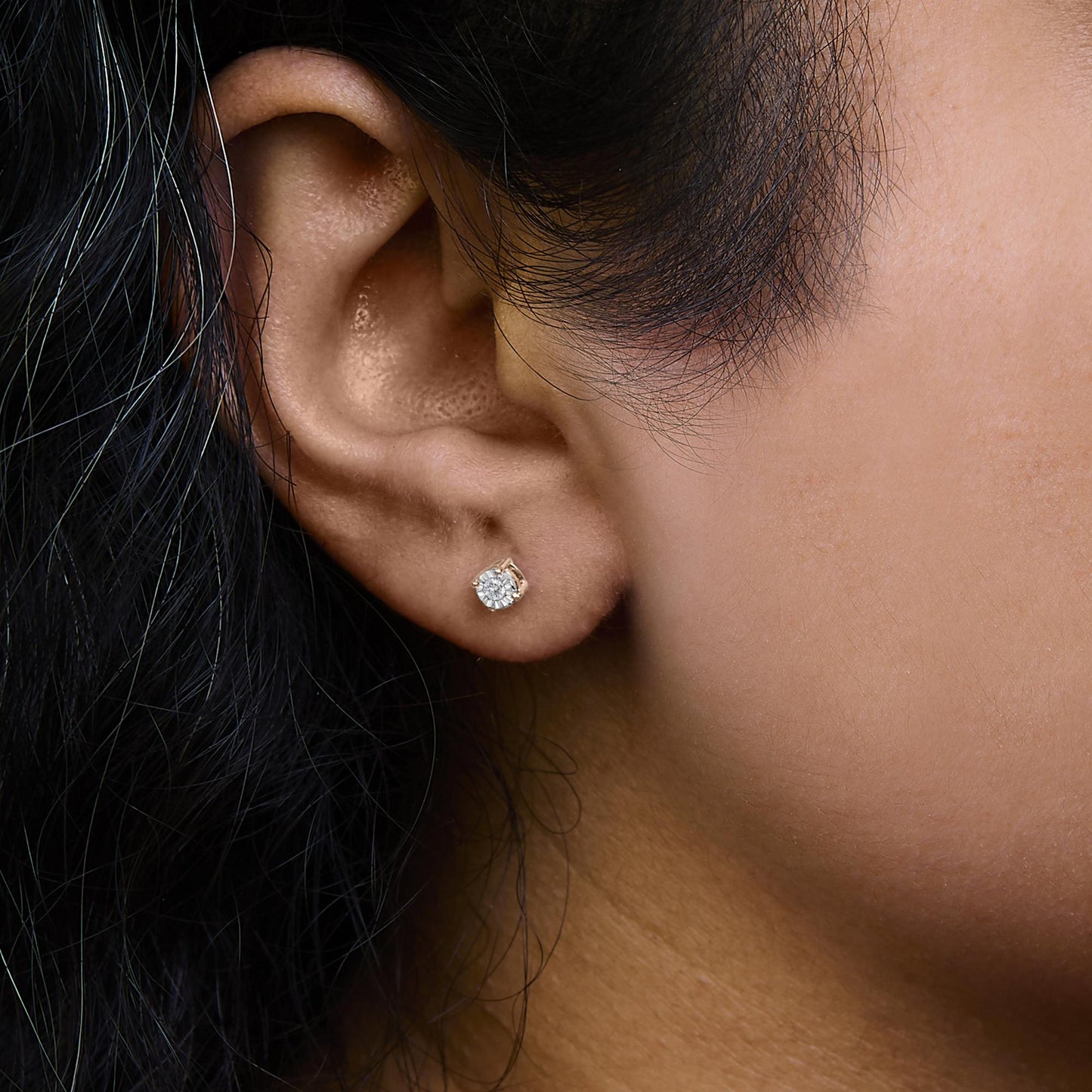 Close-up side view of a rose-colored stud earring with a round white gemstone in miracle setting, worn on a model's ear.
