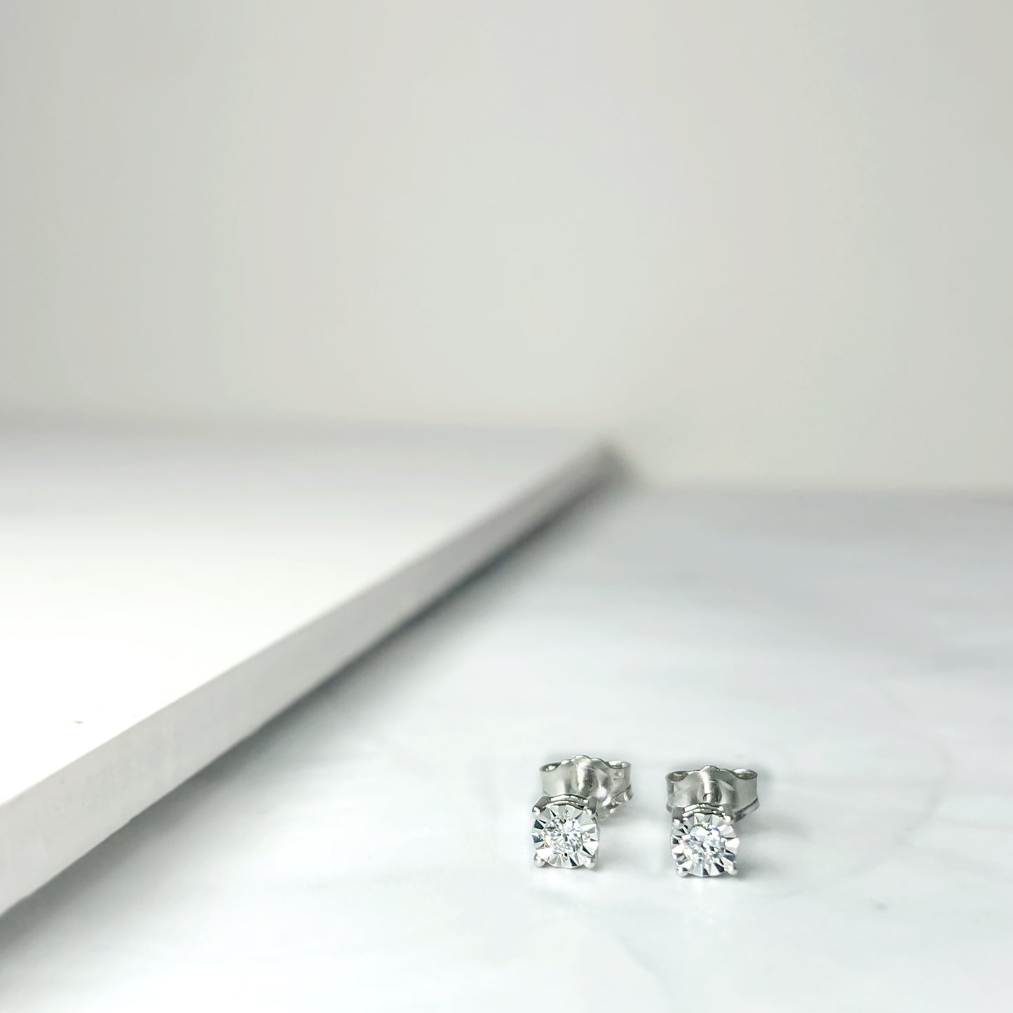 Close-up front angle of a pair of white earrings with round white gemstones in miracle settings on a flat surface.