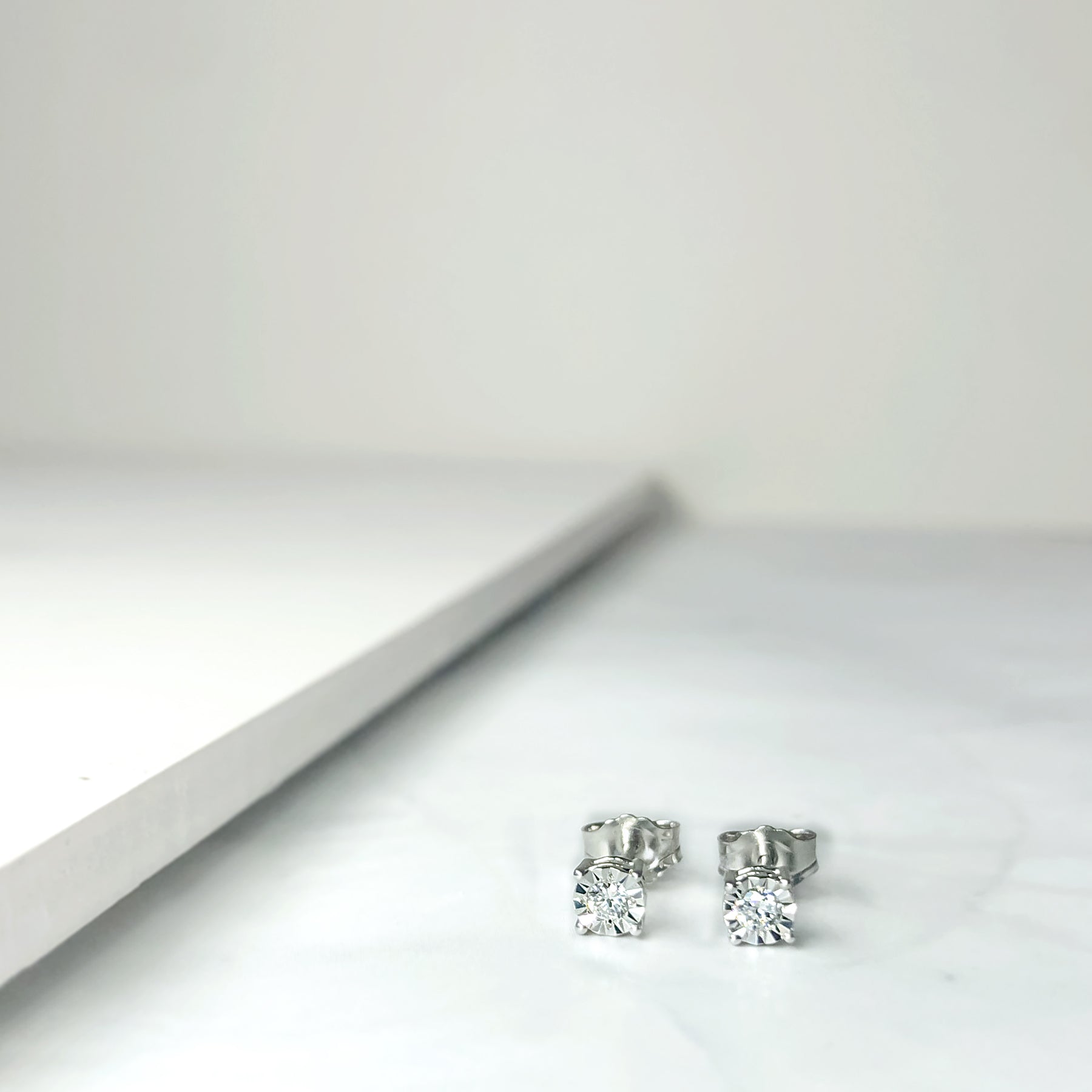 Close-up front angle of a pair of white earrings with round white gemstones in miracle settings on a flat surface.