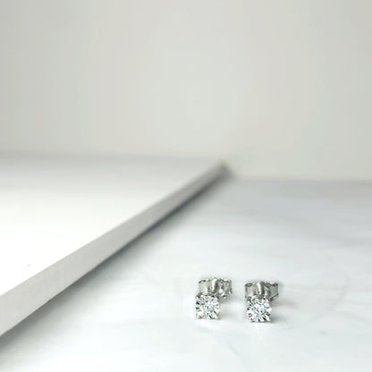Close-up front angle of a pair of white earrings with round white gemstones in miracle settings on a flat surface.