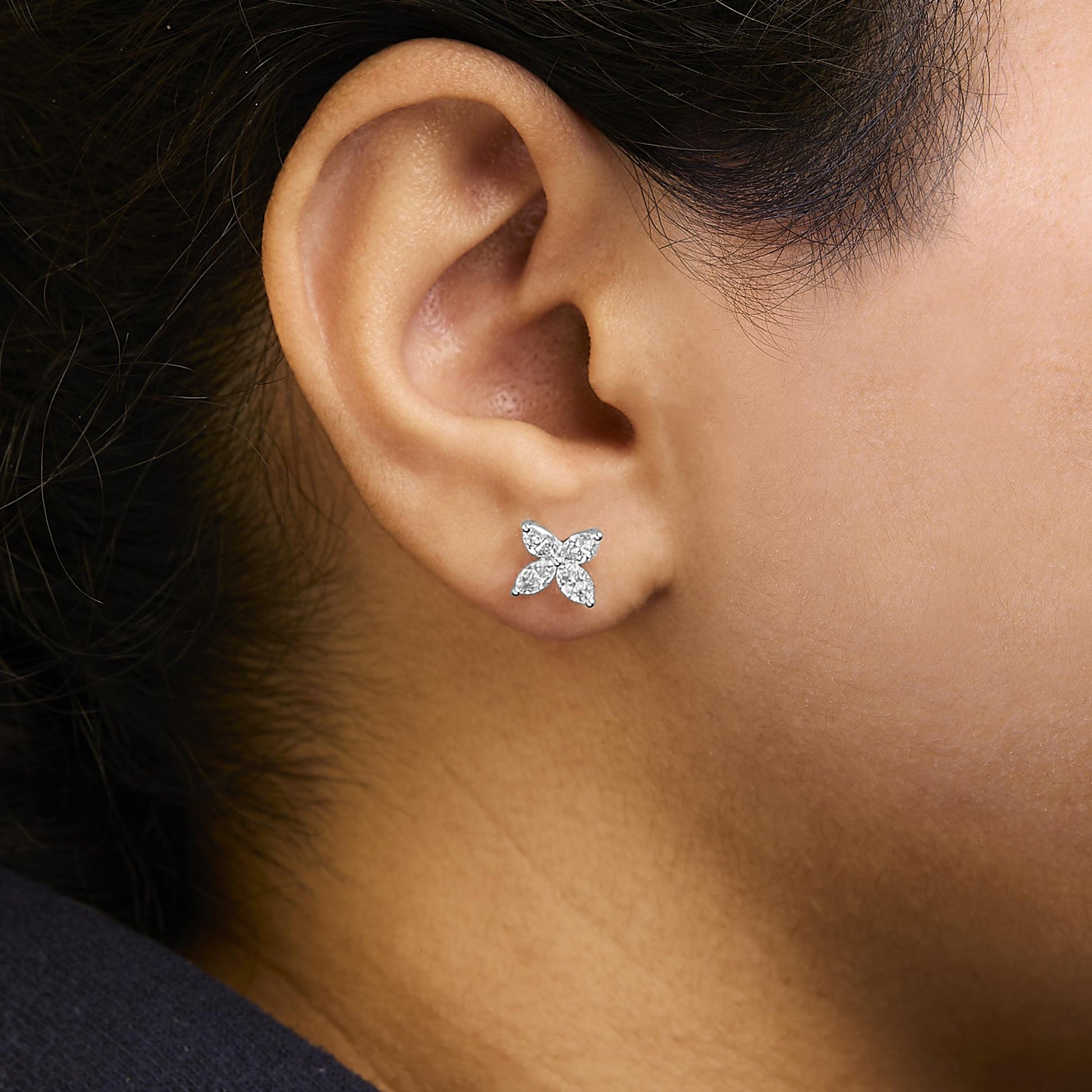 Close-up side view of a model wearing white metal stud earrings shaped like a flower with four marquise-shaped white gemstones in prong settings.