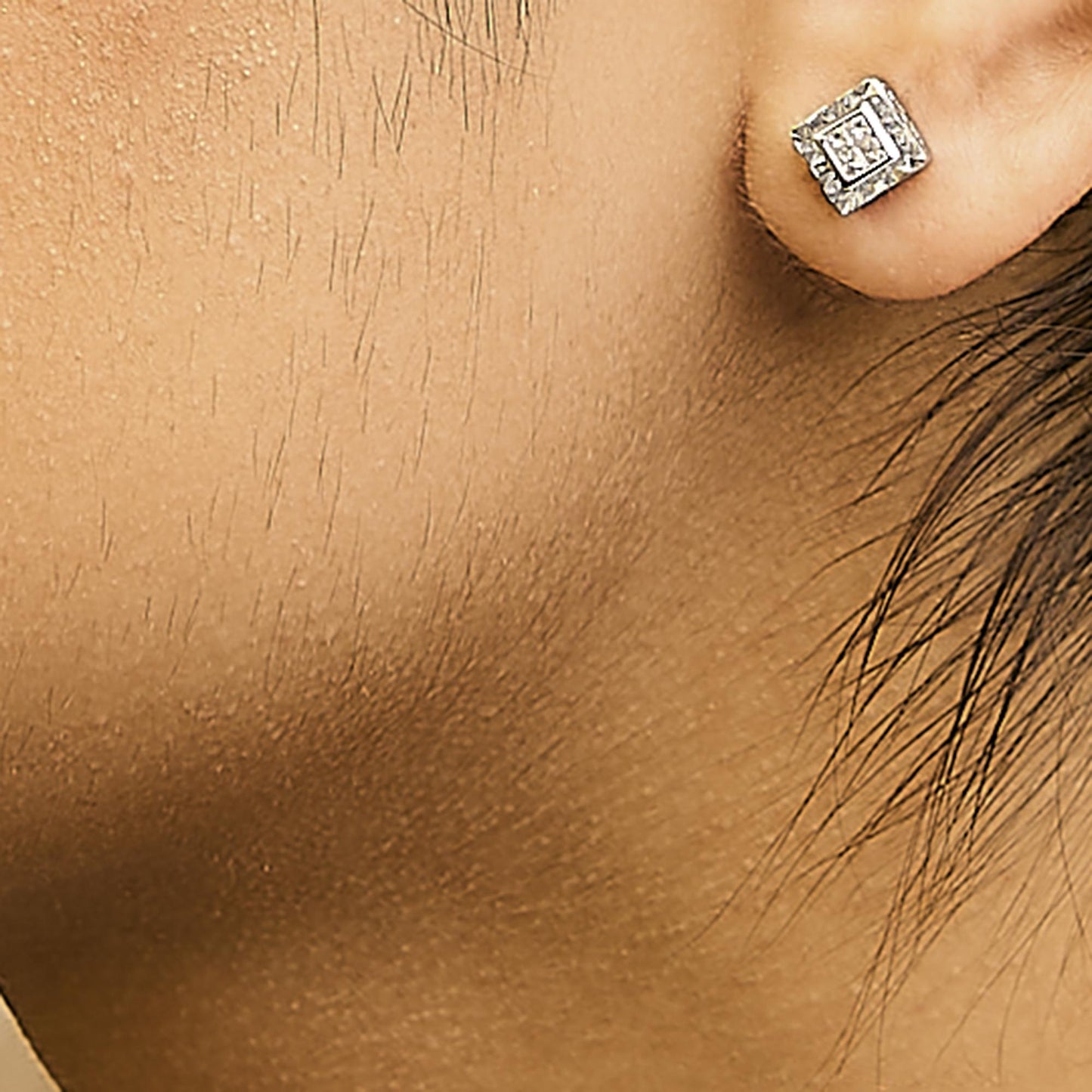Close-up side view of a model wearing a white metal square stud earring with multiple small white gemstones in a princess shape and invisible setting.