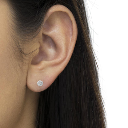 Close-up side view of a white metal stud earring with round and baguette shaped white gemstones, worn on a model's ear.