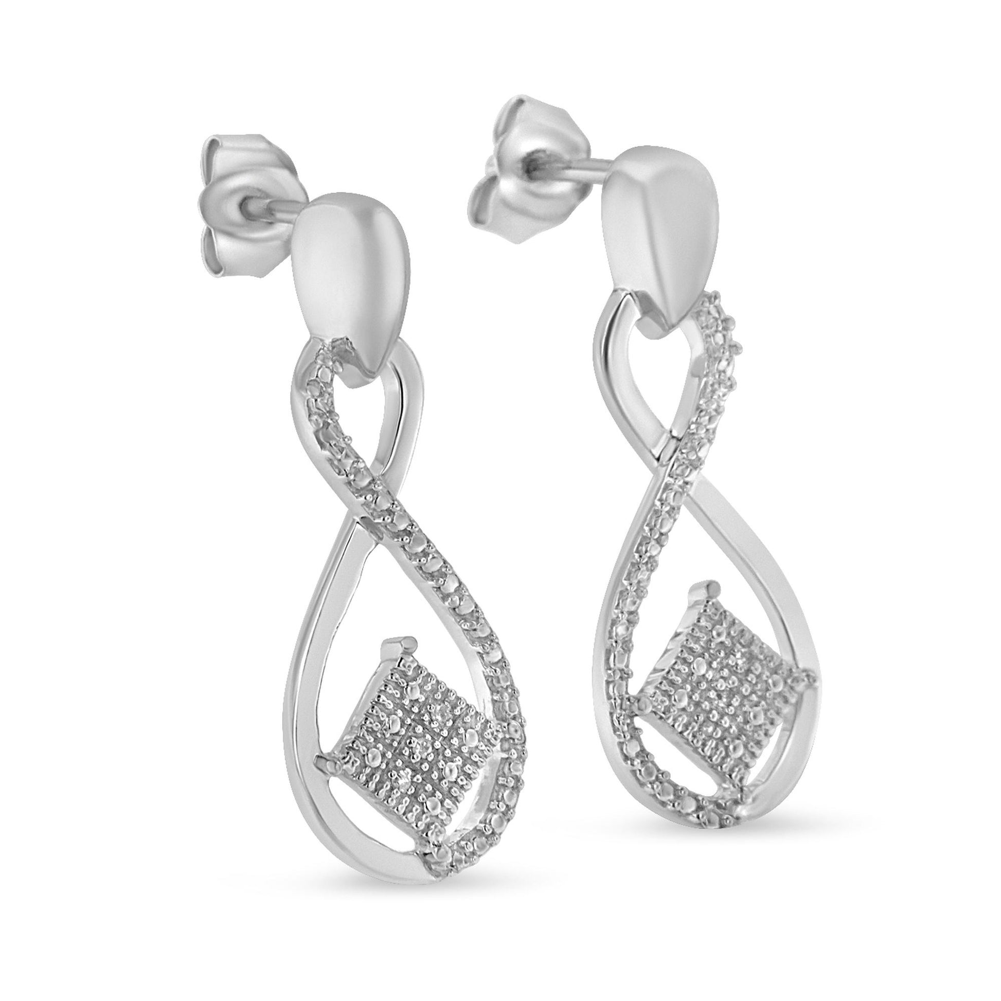 Side angle view of white metal dangle earrings with an infinity shape, featuring a row of small white gemstones in a pave setting along one side and a cluster of white gemstones set in a square shape near the bottom.