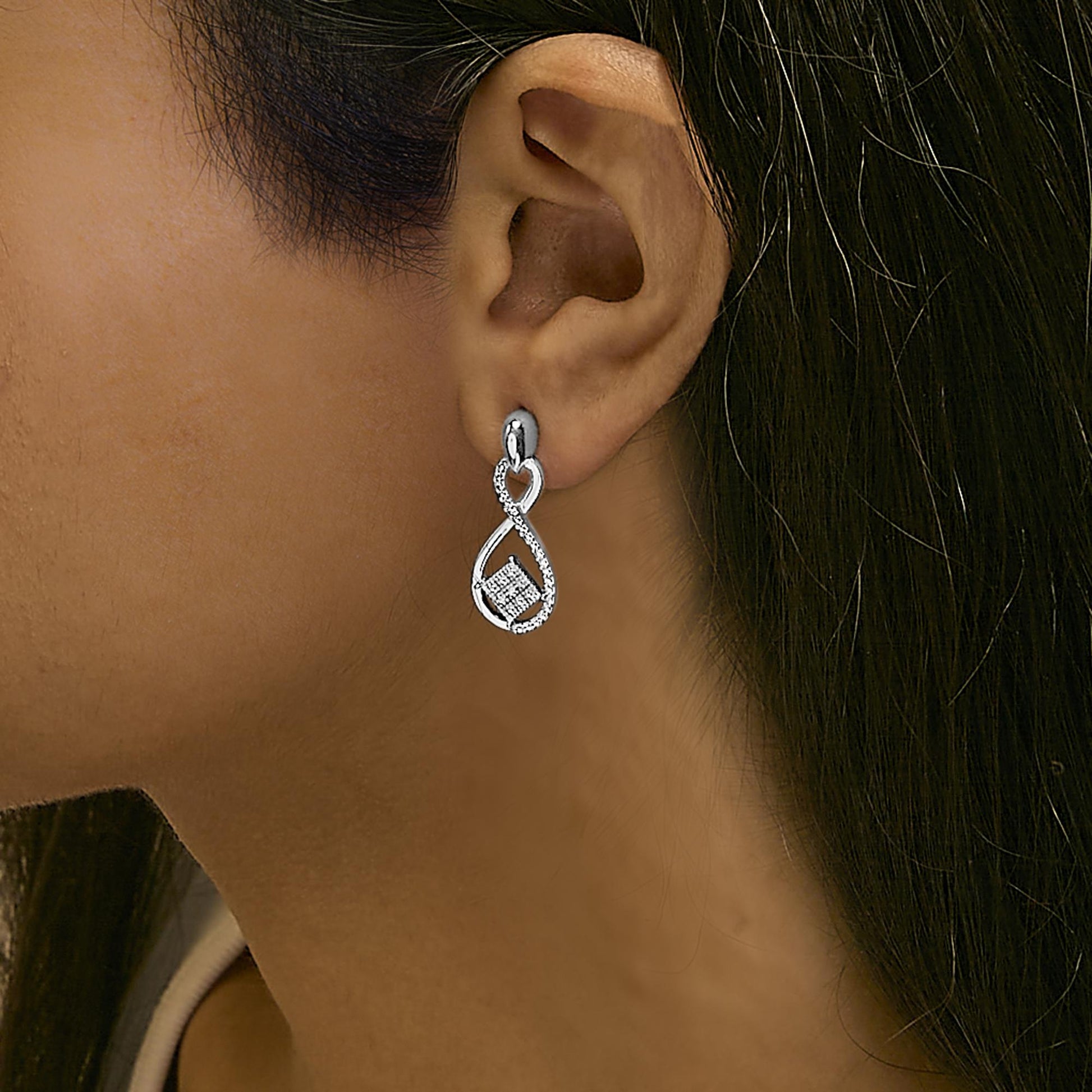 Side view of a white metal infinity-shaped earring with round white gemstones in pave setting, worn on a model.