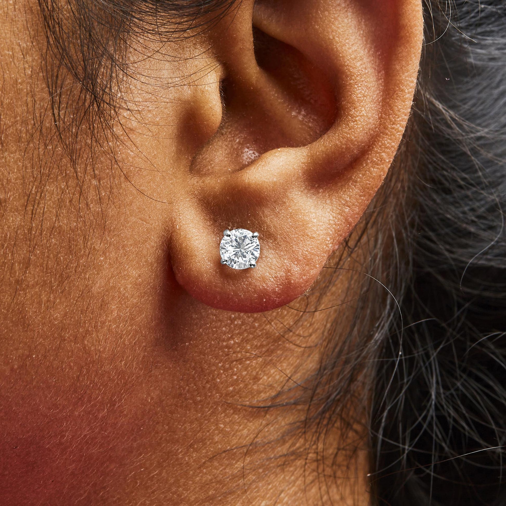 Close-up side view of a white metal stud earring with a round white gemstone in a four-prong setting worn on a model.
