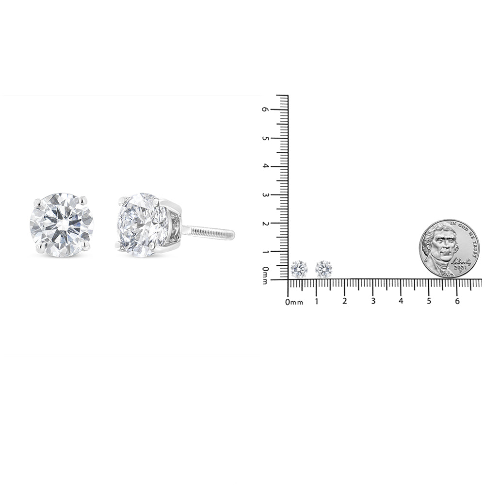 White metal stud earrings with round white gemstones in 4-prong settings, shown in a close-up side and front angle, placed next to a ruler and coin for size reference.