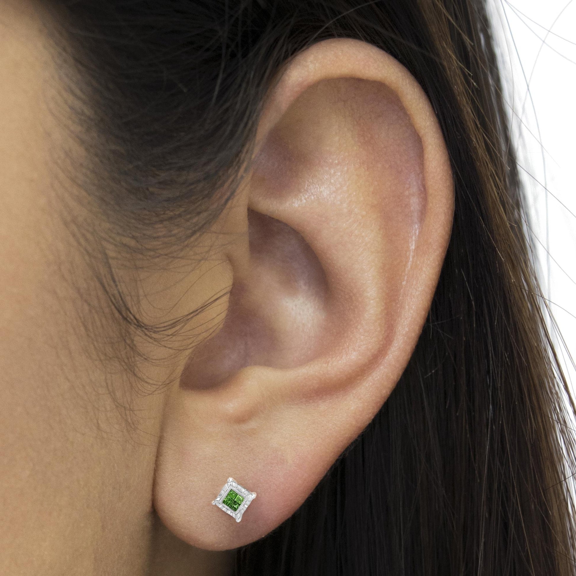 Close-up side view of an ear wearing a white metal stud earring with a square invisible setting and a green princess-shaped gemstone.